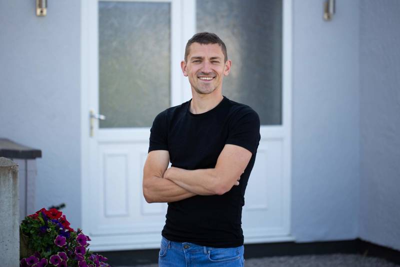 A man standing in front of his house smiling with arms crossed
