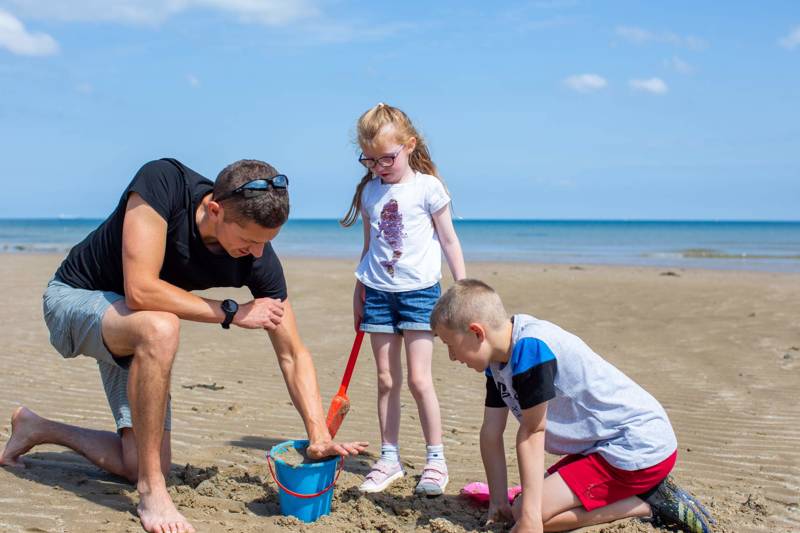 Dad helping his two children build a sandcastle on the beach